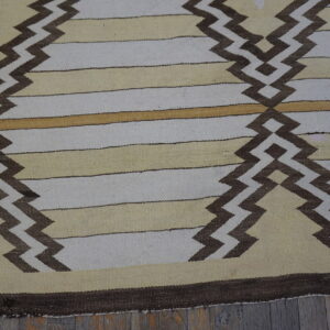 Flatweave rug with beige, white, and gold stripes, accented by dark brown geometric zigzag patterns on wood.