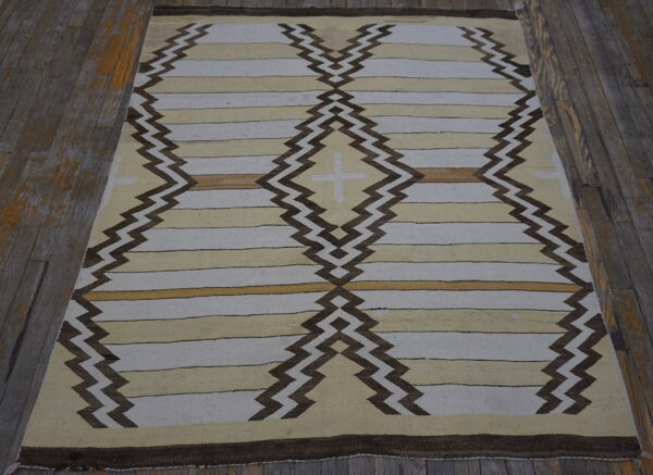 Cream and tan striped flatweave rug features dark brown zigzag columns forming central diamonds on wooden floors.