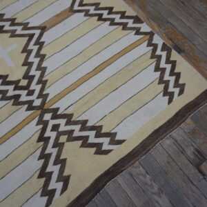 Cream and yellow flatweave rug featuring brown zigzag patterns over distressed wood flooring.
