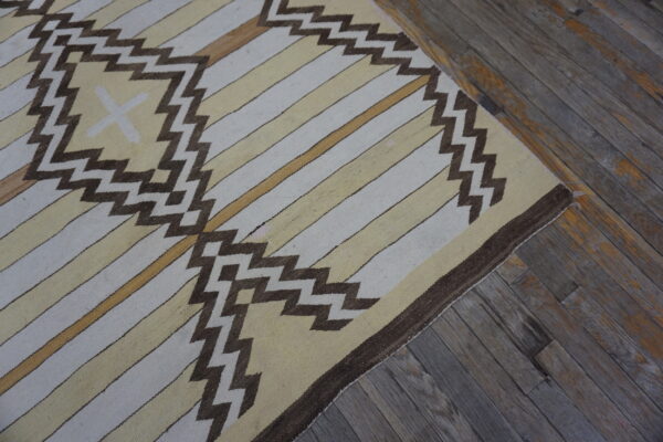 Cream and yellow flatweave rug featuring brown zigzag patterns over distressed wood flooring.