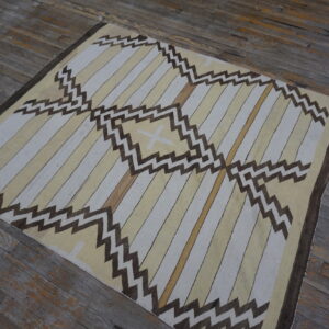 Geometric flatweave rug with light stripes and dark brown zigzags displayed on weathered hardwood floors.