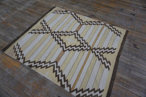 Geometric flatweave rug with light stripes and dark brown zigzags displayed on weathered hardwood floors.
