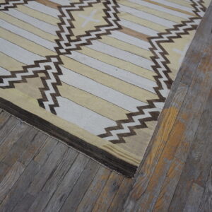 Flat-woven rug featuring beige and white stripes, brown zigzag motifs, resting on rustic gray wood floors.