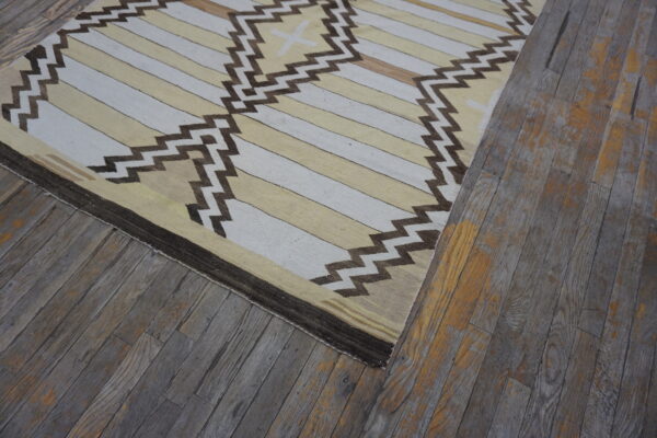 Flat-woven rug featuring beige and white stripes, brown zigzag motifs, resting on rustic gray wood floors.