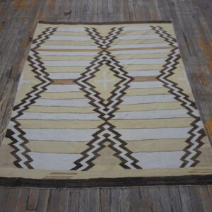 Tan and white flatweave rug with dark brown zig-zag diamonds rests on rustic gray wood flooring.