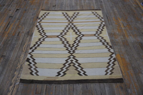Tan and white flatweave rug with dark brown zig-zag diamonds rests on rustic gray wood flooring.