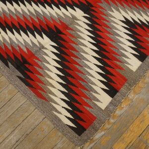 Red, black, cream, and gray jagged diamond rug lies diagonally on distressed wood planks.