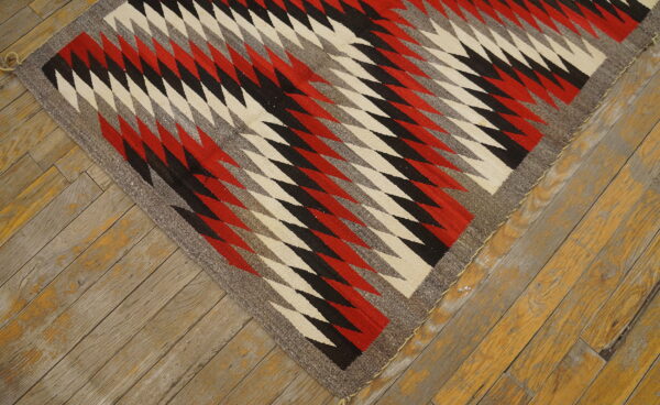 Bold tribal geometric pattern antique native american flat weave navajo rug 2 Red, black, cream, and gray jagged diamond rug lies diagonally on distressed wood planks.