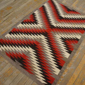 Flatwoven rug displaying red, black, cream, and grey zigzagging geometric patterns on weathered wood flooring.