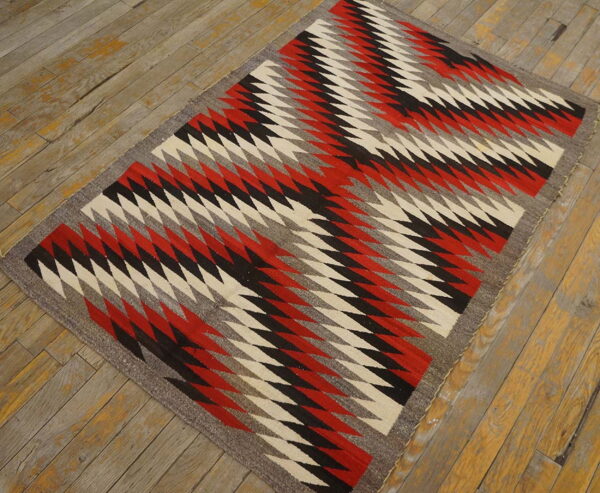 Bold tribal geometric pattern antique native american flat weave navajo rug 3 Flatwoven rug displaying red, black, cream, and grey zigzagging geometric patterns on weathered wood flooring.