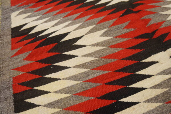 Bold tribal geometric pattern antique native american flat weave navajo rug 5 A flat-woven rug displays red, black, cream, and gray geometric diamond shapes with a solid border.