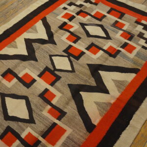 Low-pile rug with bold red, black, and cream diamonds over a gray field on wooden flooring.