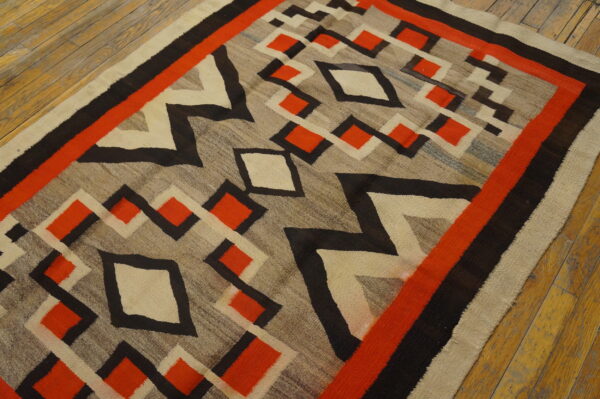 Low-pile rug with bold red, black, and cream diamonds over a gray field on wooden flooring.