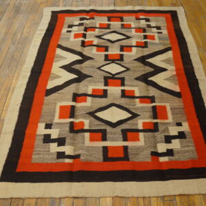Geometric low-pile rug in orange, black, gray, and beige colors lies on light wooden floorboards.