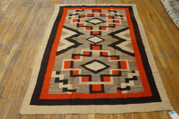 Geometric low-pile rug in orange, black, gray, and beige colors lies on light wooden floorboards.