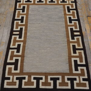 Flatweave rug with a gray center and a dark brown, tan, and cream geometric key border.
