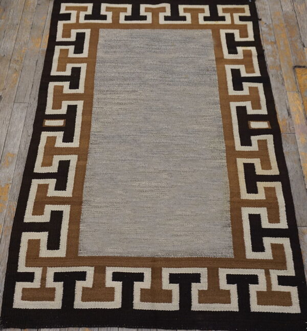 Flatweave rug with a gray center and a dark brown, tan, and cream geometric key border.