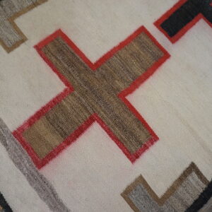 Geometric flatweave rug in cream, brown, red, and black with angular designs on distressed wood plank flooring.