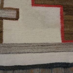 Flatwoven rug detail showing cream, brown, and red geometric pattern over rustic wooden flooring.