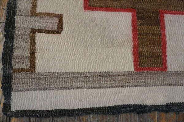 Flatwoven rug detail showing cream, brown, and red geometric pattern over rustic wooden flooring.
