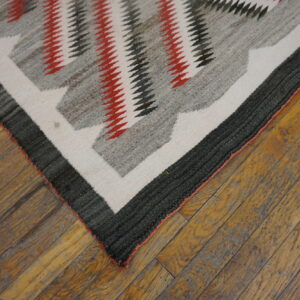 Geometric flatweave rug in red, charcoal, gray, and cream resting on worn wooden planks.