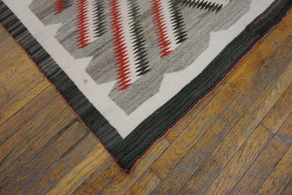 Geometric flatweave rug in red, charcoal, gray, and cream resting on worn wooden planks.