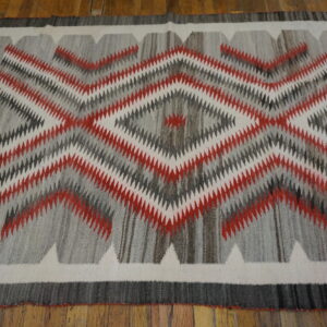 Red, white, and charcoal rug featuring serrated diamond patterns lies flat on wood planks.