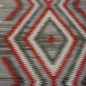 Low-pile rug with a red, white, and gray zig-zag geometric pattern on wood flooring.