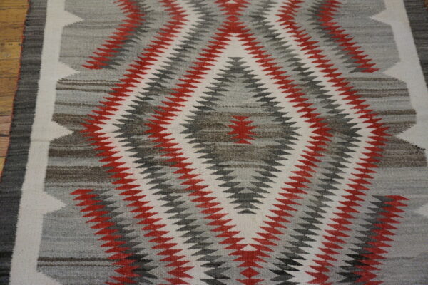 Low-pile rug with a red, white, and gray zig-zag geometric pattern on wood flooring.