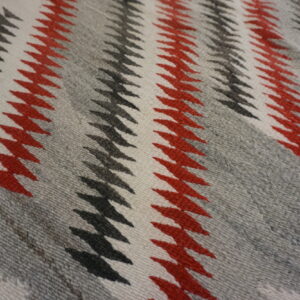 A close-up of a rug featuring red, black, white, and gray zig-zag stripe patterns.