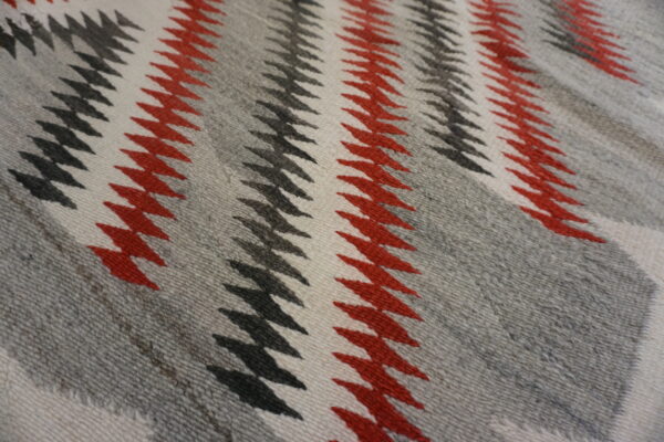 A close-up of a rug featuring red, black, white, and gray zig-zag stripe patterns.
