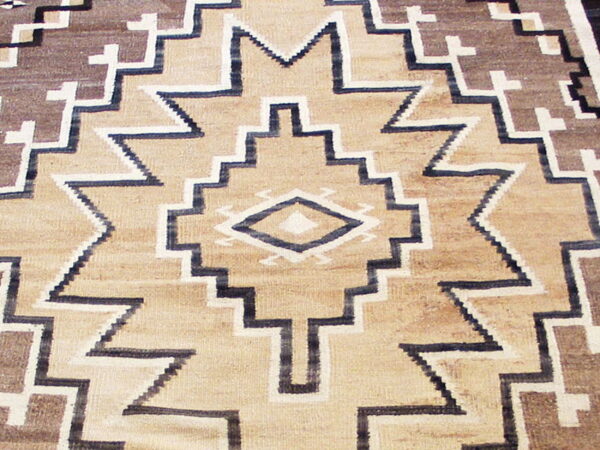 Flatweave rug detail with stepped geometric patterns in tan, brown, cream, and dark blue.