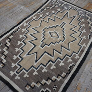 A tan and brown geometric rug with zigzag patterns rests on distressed gray wood flooring.