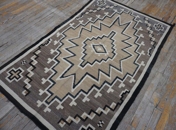 A tan and brown geometric rug with zigzag patterns rests on distressed gray wood flooring.