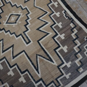 Flat-woven rug with tan, brown, and charcoal geometric zigzag patterns on rustic wood floor.