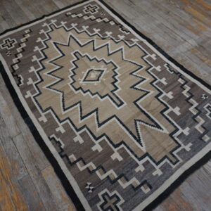 Tan, brown, and black geometric rug rests on heavily weathered gray and yellow wooden plank flooring.