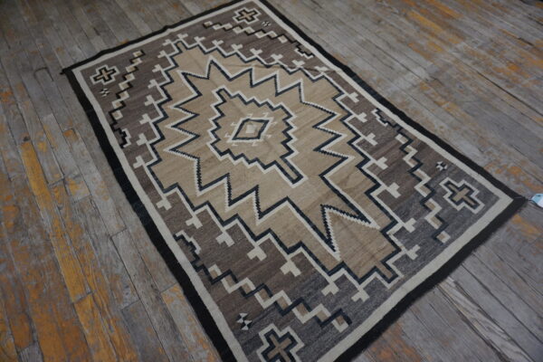 Tan, brown, and black geometric rug rests on heavily weathered gray and yellow wooden plank flooring.