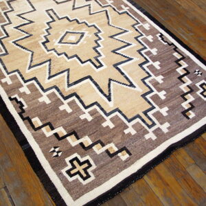 Geometric area rug in shades of tan, brown, black, and white on a glossy wood plank floor.