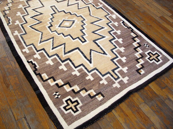 Geometric area rug in shades of tan, brown, black, and white on a glossy wood plank floor.