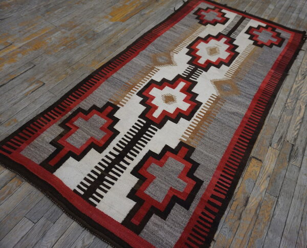 Red, gray, and brown flatweave rug with a central stepped geometric design rests on rustic wood planks.