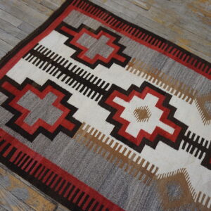 Low-pile rug in geometric stripes of grey, white, red, and dark brown on distressed wood flooring.