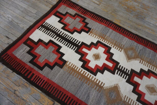Low-pile rug in geometric stripes of grey, white, red, and dark brown on distressed wood flooring.