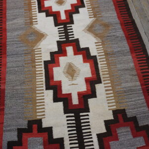 Flat-woven rug with red, black, white, and gray geometric designs on distressed wooden flooring.