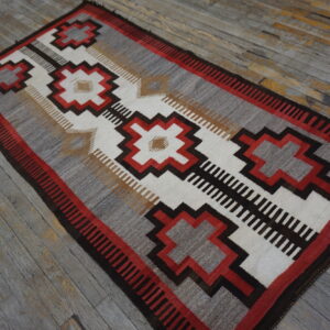 Flatwoven geometric rug in red, dark brown, white, and gray on distressed wood flooring.