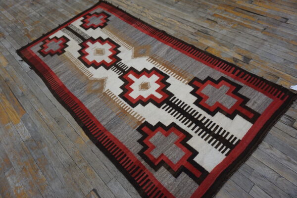 Flatwoven geometric rug in red, dark brown, white, and gray on distressed wood flooring.