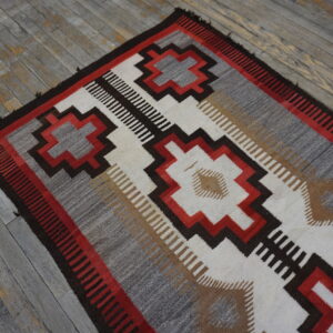 Flatweave rug with stepped red, gray, and brown geometric designs lying on weathered gray wood floor.