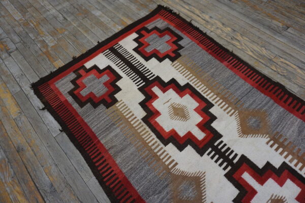 Flatweave rug with stepped red, gray, and brown geometric designs lying on weathered gray wood floor.