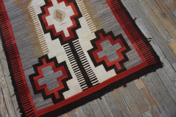 Geometric rug in gray, red, cream, and dark brown placed on weathered gray wooden flooring.