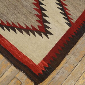 Flatwoven rug corner displays red, brown, and tan geometric zigzag patterns over distressed wood flooring.
