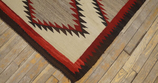 Flatwoven rug corner displays red, brown, and tan geometric zigzag patterns over distressed wood flooring.